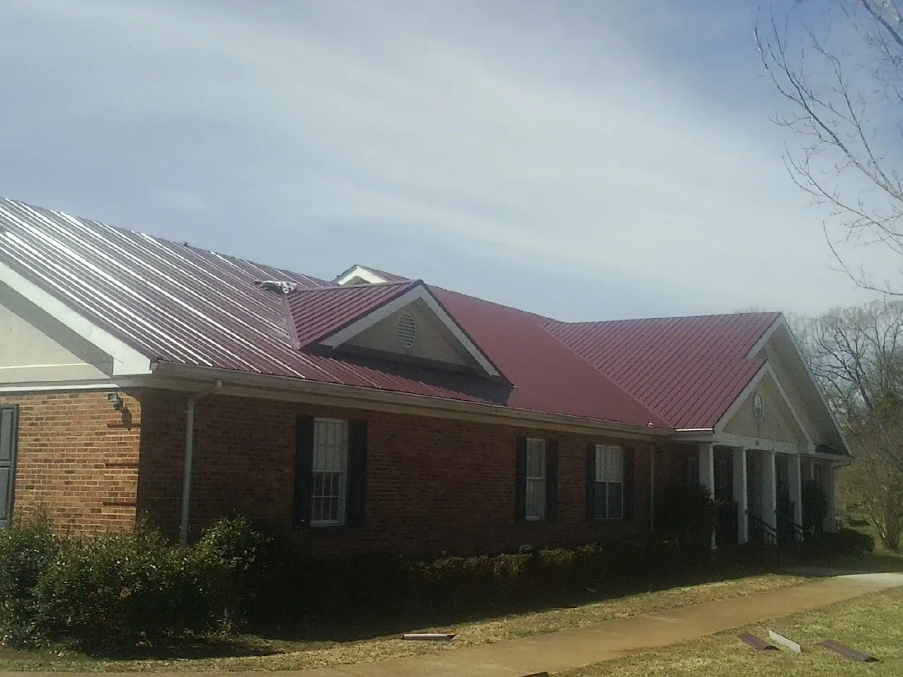 Red metal roof with gabled entries on a long brick building, from a Hail Damage Roof Repair job in Warren